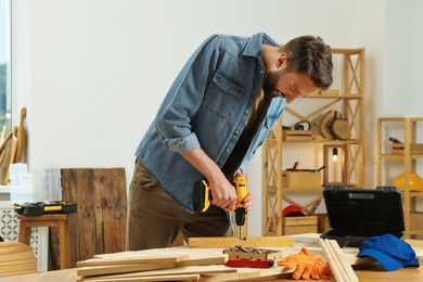 Photo of Craftsman working with drill at wooden table in workshop