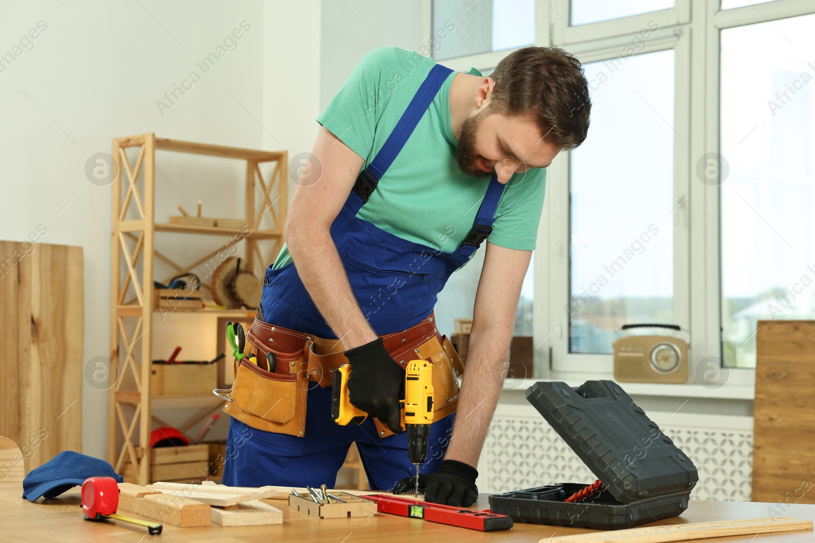 Photo of Craftsman working with drill at wooden table in workshop