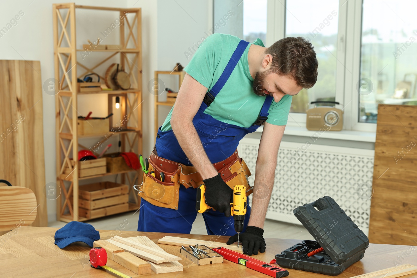 Photo of Craftsman working with drill at wooden table in workshop