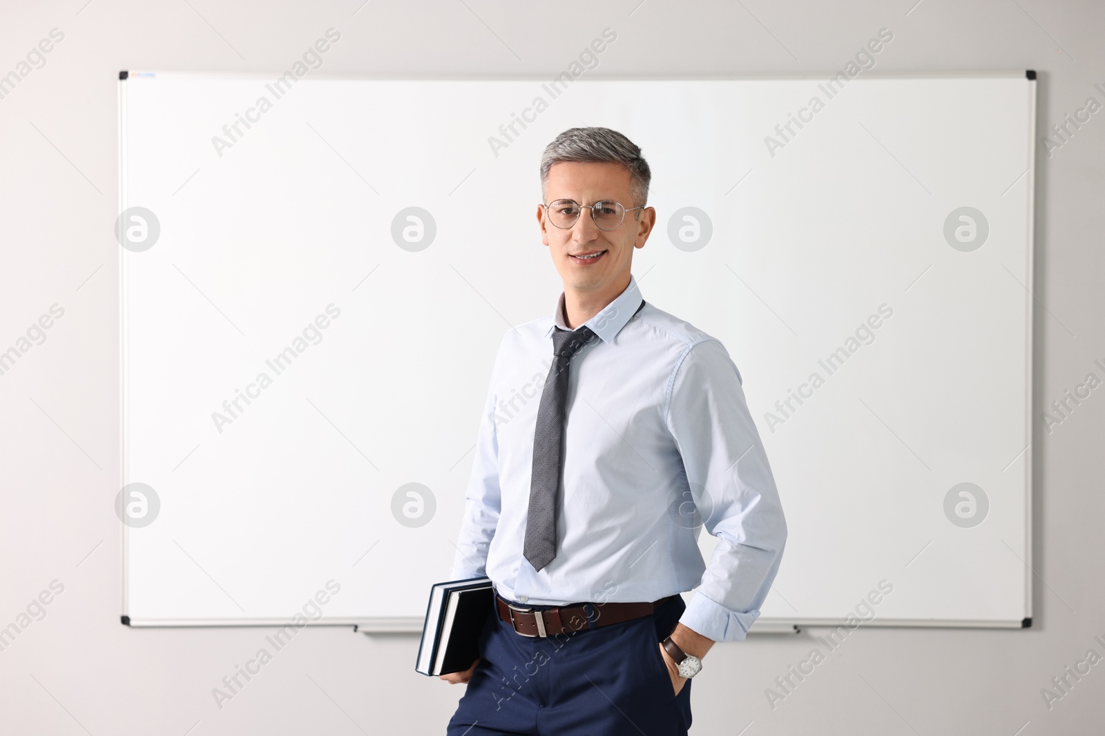 Photo of Teacher with notebooks near whiteboard in classroom