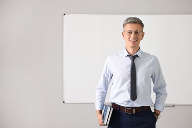 Photo of Teacher with notebooks near whiteboard in classroom, space for text