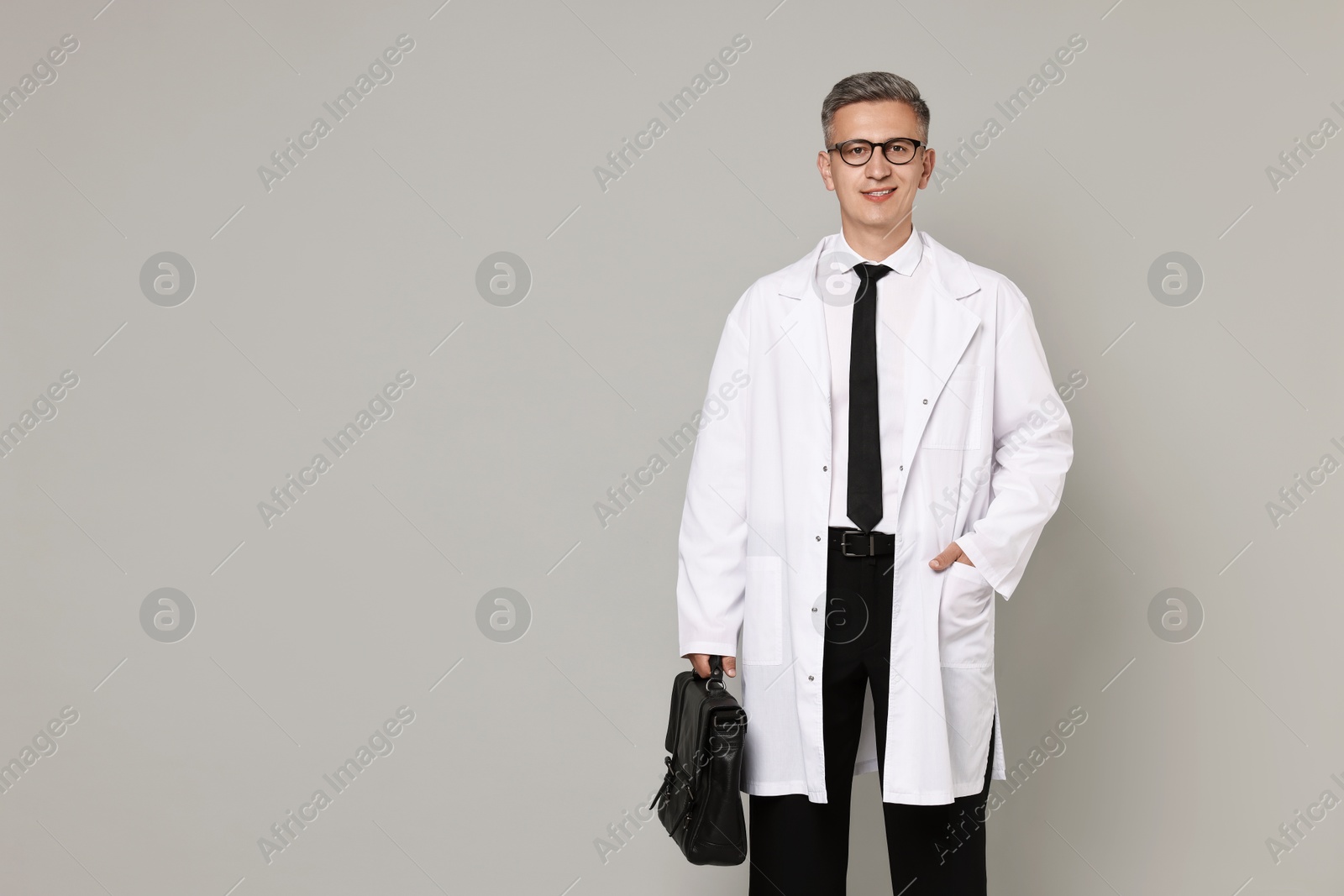 Photo of Doctor in glasses holding briefcase on grey background, space for text