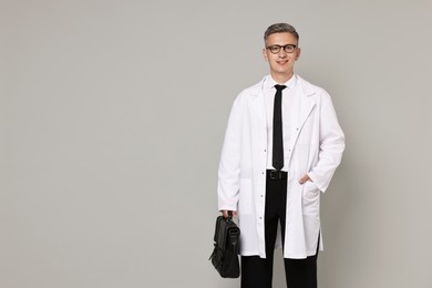 Doctor in glasses holding briefcase on grey background, space for text