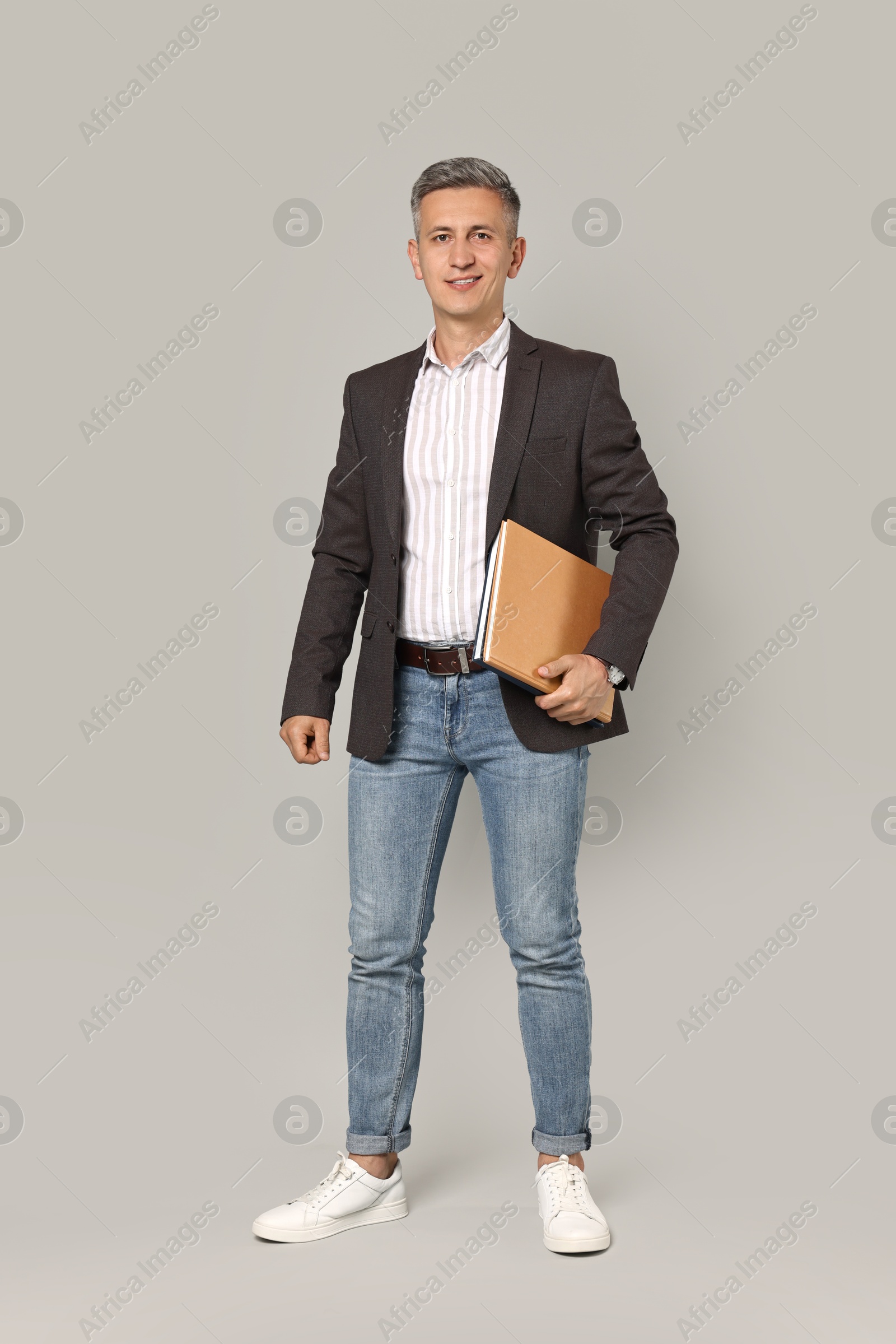 Photo of Happy teacher with notebooks on grey background