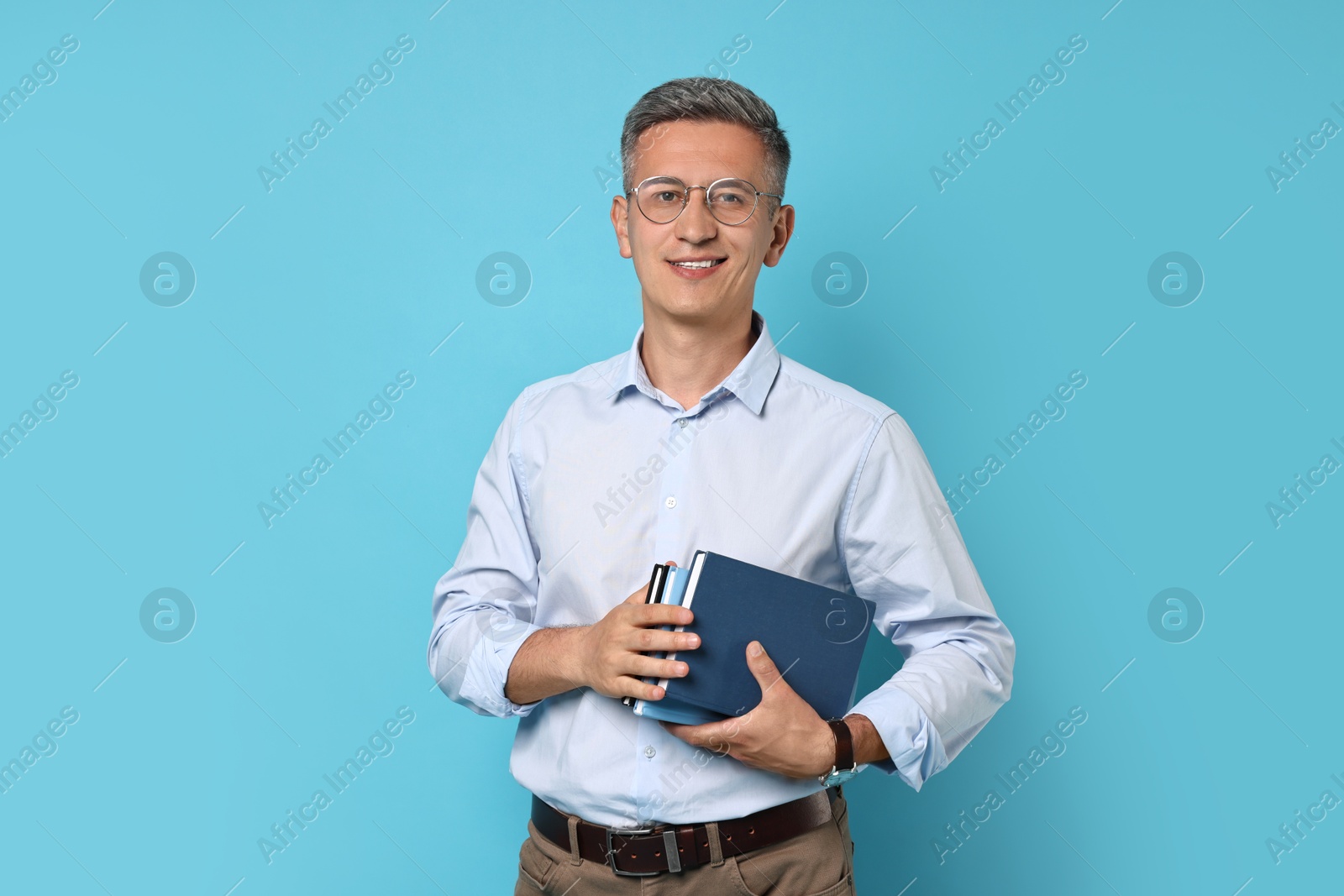 Photo of Teacher in glasses holding books on light blue background