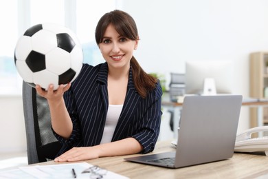 Smiling employee with soccer ball at table in office