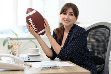 Smiling employee with american football ball at table in office