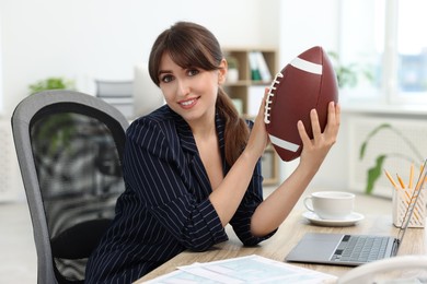 Smiling employee with american football ball at table in office