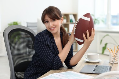 Photo of Smiling employee with american football ball at table in office