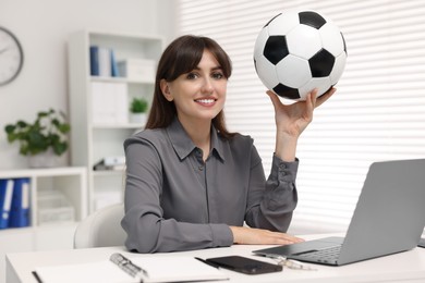 Smiling employee with soccer ball at table in office