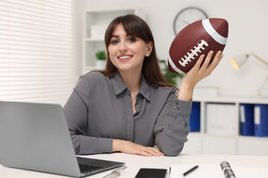 Photo of Smiling employee with american football ball at table in office