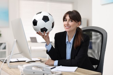 Smiling employee with soccer ball at table in office