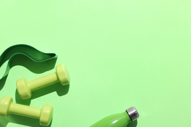 Photo of Dumbbells, fitness elastic band and water bottle on light green background, flat lay. Space for text