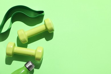 Dumbbells, fitness elastic band and water bottle on light green background, flat lay. Space for text