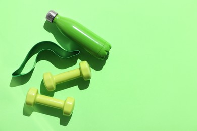 Photo of Dumbbells, fitness elastic band and water bottle on light green background, flat lay. Space for text