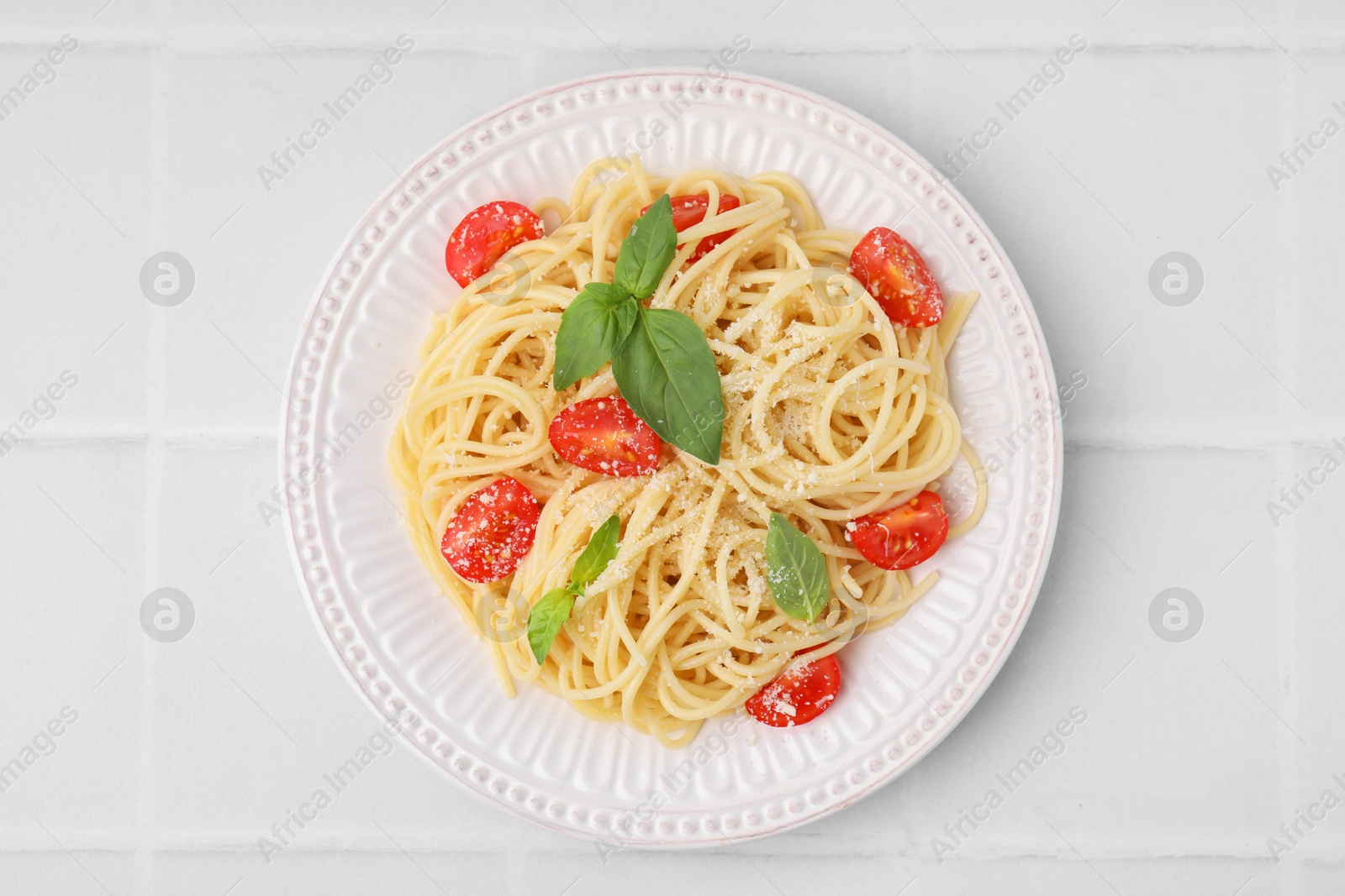 Photo of Tasty pasta with tomato, cheese and basil on white tiled table, top view