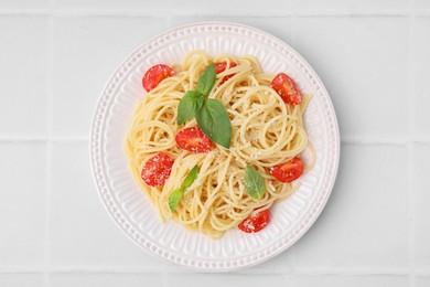 Tasty pasta with tomato, cheese and basil on white tiled table, top view