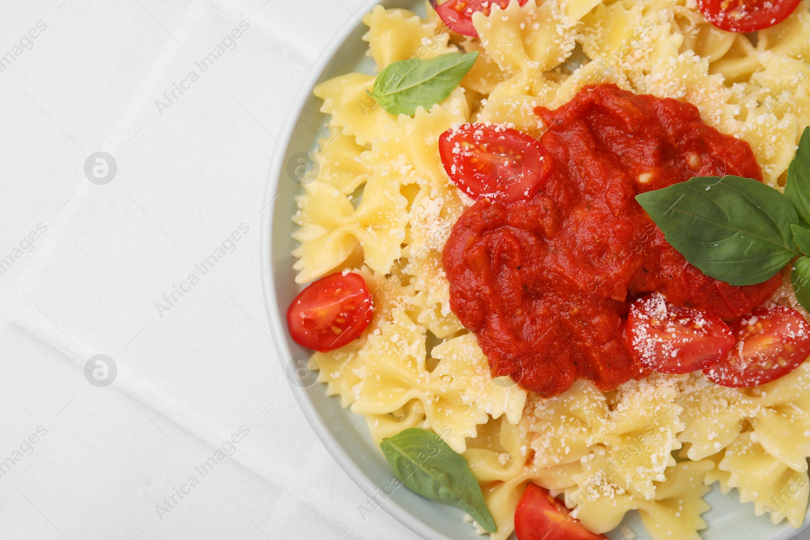 Photo of Tasty pasta with tomato sauce, cheese and basil on white tiled table, top view. Space for text