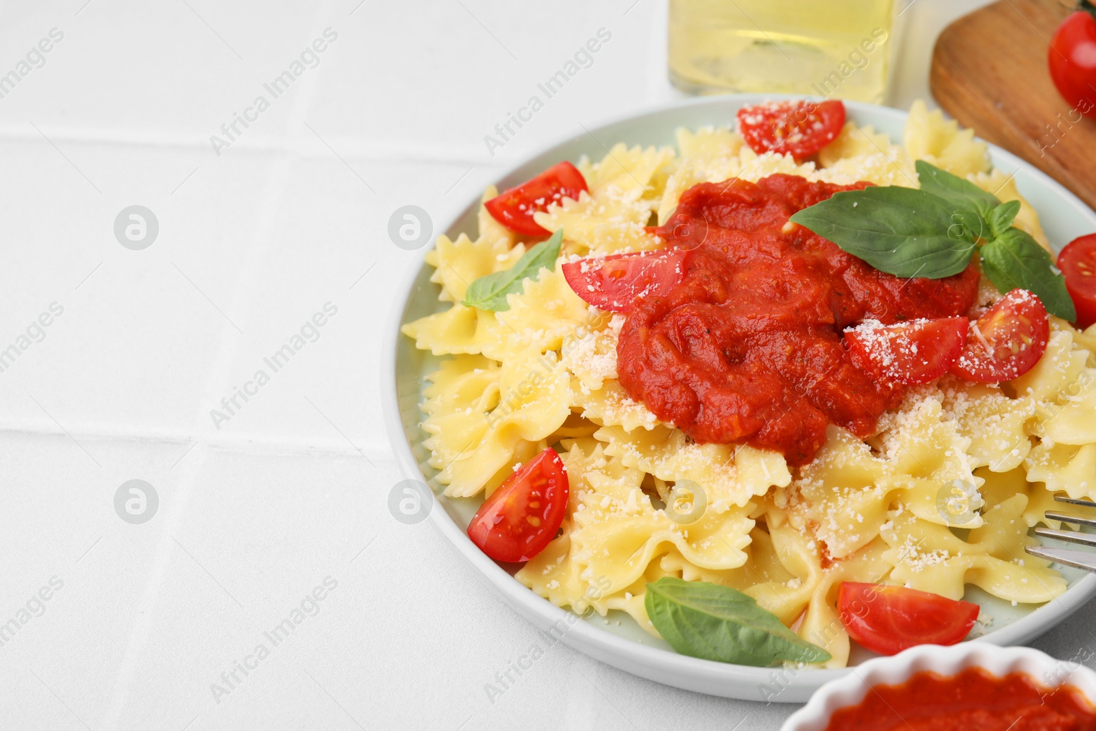 Photo of Tasty pasta with tomato sauce, cheese and basil on white tiled table, closeup. Space for text