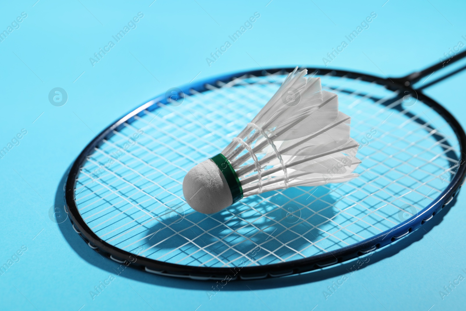 Photo of Feather badminton shuttlecock and racket on light blue background, closeup