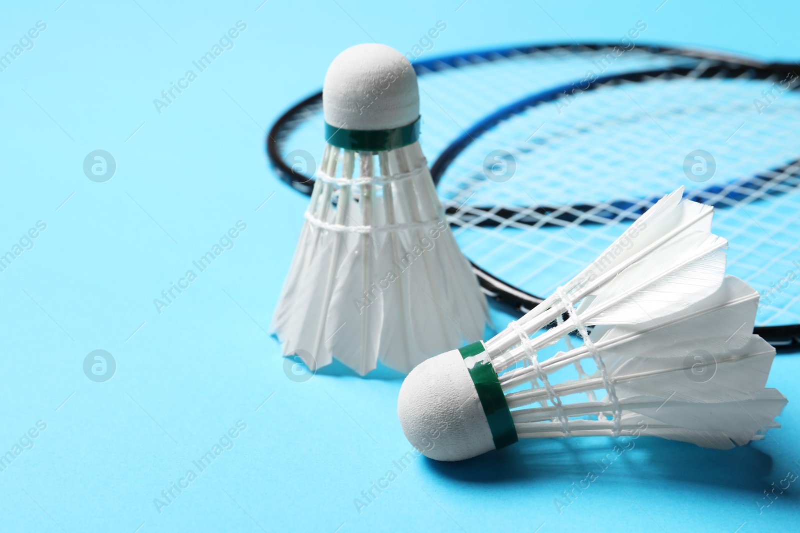 Photo of Feather badminton shuttlecocks and rackets on light blue background, closeup. Space for text