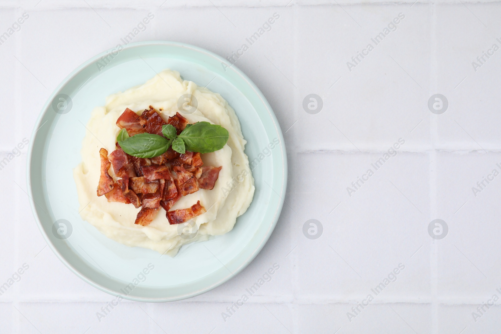 Photo of Fried bacon, mashed potato and basil on white tiled table, top view. Space for text