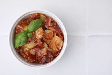 Delicious baked potatoes, bacon and basil in bowl on white table, top view. Space for text