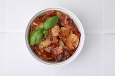 Delicious baked potatoes, bacon and basil in bowl on white table, top view