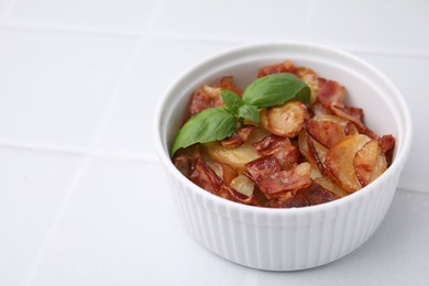 Delicious baked potatoes, bacon and basil in bowl on white table, space for text