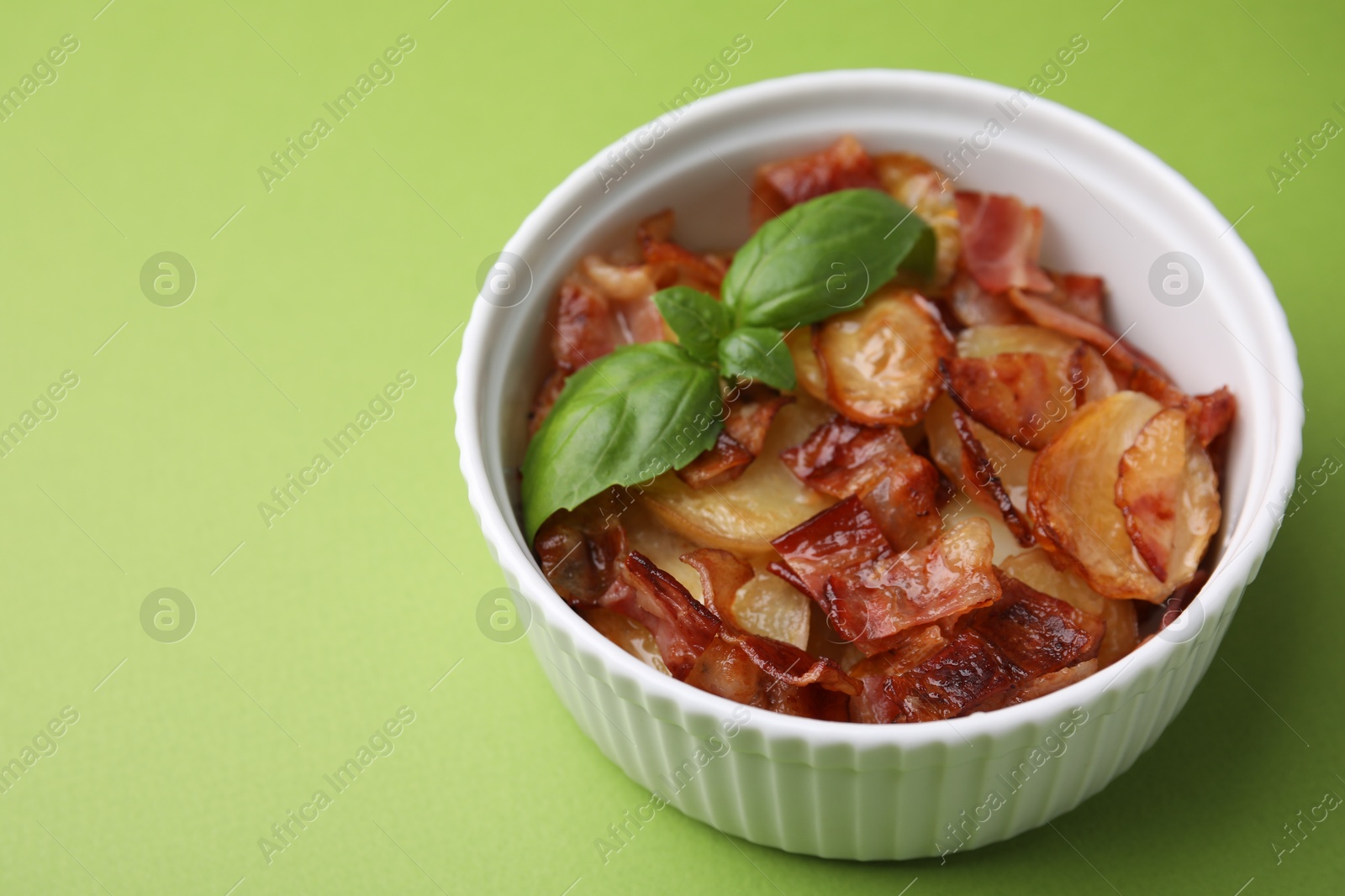 Photo of Delicious baked potatoes, bacon and basil in bowl on green background, closeup. Space for text