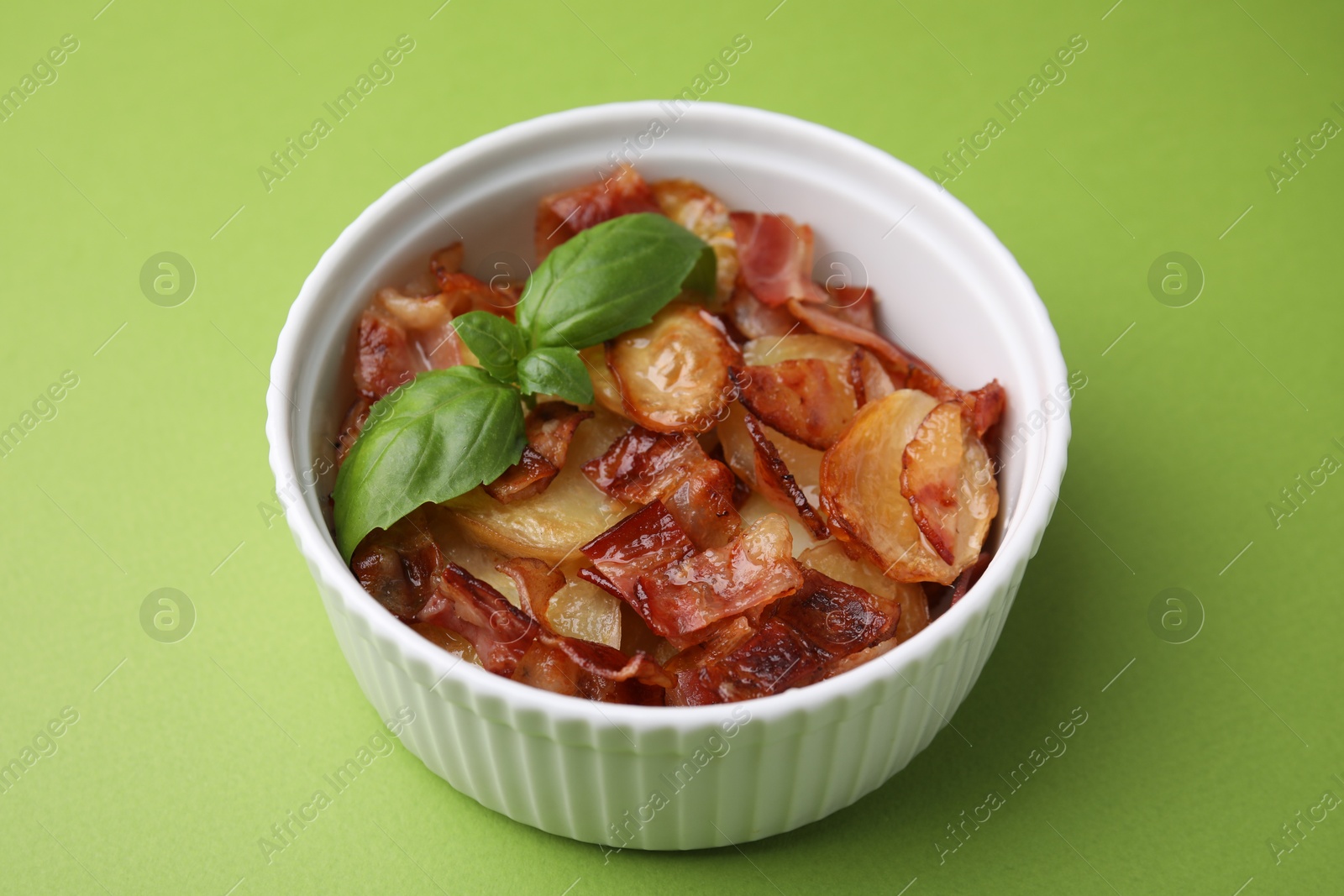 Photo of Delicious baked potatoes, bacon and basil in bowl on green background