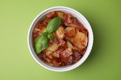 Delicious baked potatoes, bacon and basil in bowl on green background, top view