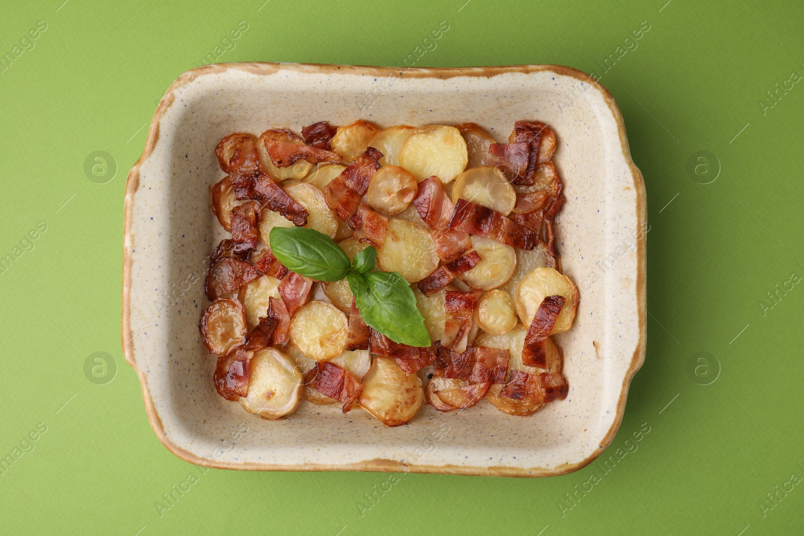 Photo of Delicious baked potatoes, bacon and basil in baking dish on green background, top view