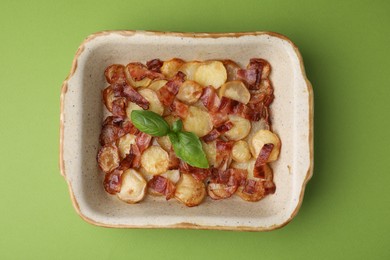 Delicious baked potatoes, bacon and basil in baking dish on green background, top view