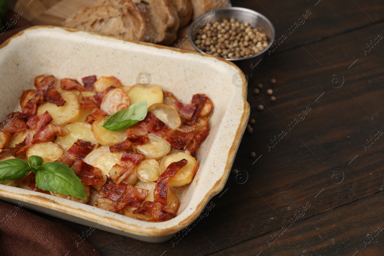 Photo of Delicious baked potatoes, bacon, basil, peppercorns and bread on wooden table, space for text