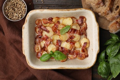 Delicious baked potatoes, bacon, basil, peppercorns and bread on wooden table, top view