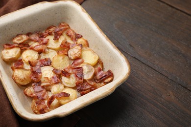 Delicious baked potatoes and bacon in baking dish on wooden table, space for text