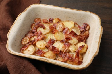 Delicious baked potatoes and bacon in baking dish on wooden table