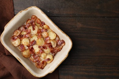 Delicious baked potatoes and bacon in baking dish on wooden table, top view. Space for text