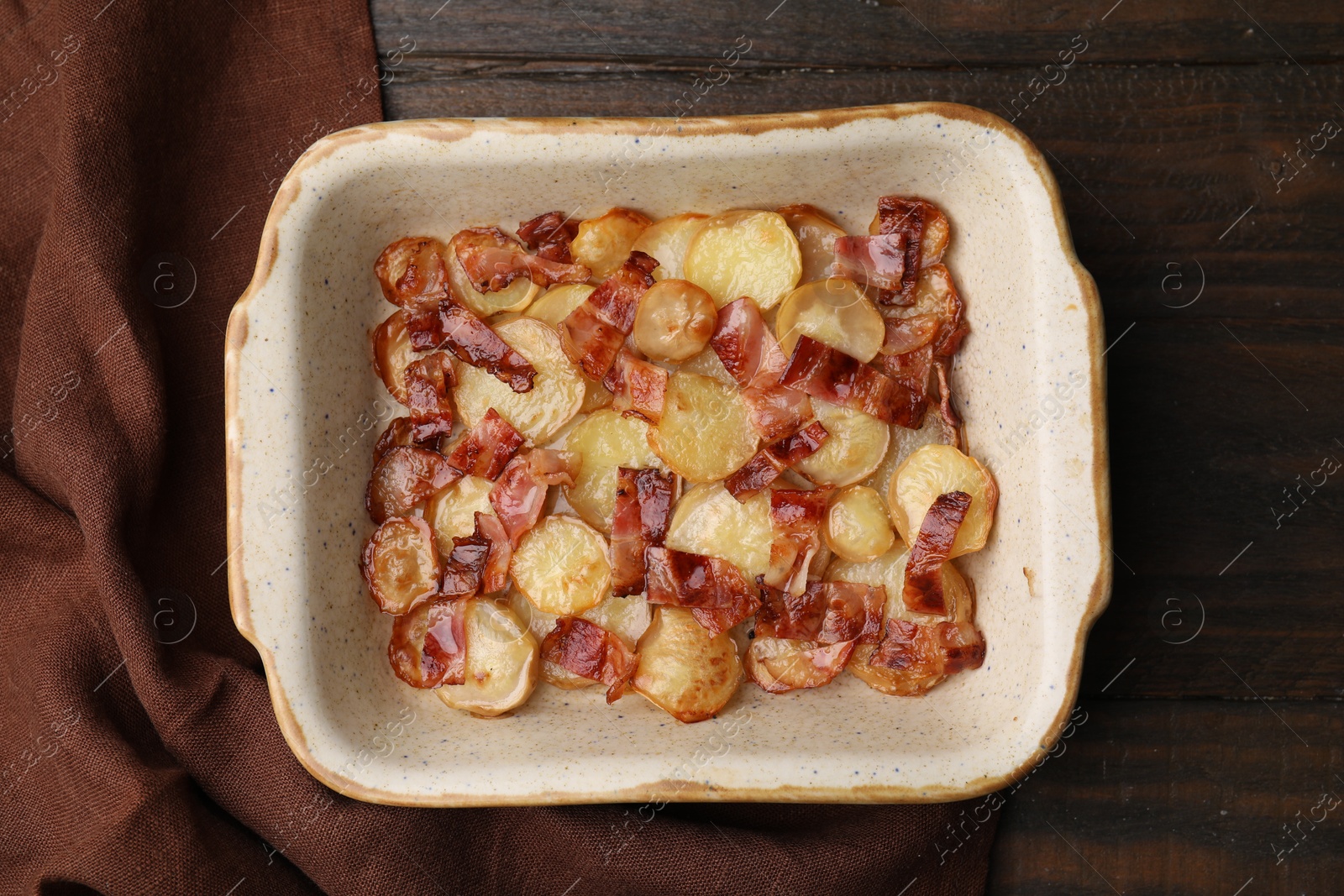 Photo of Delicious baked potatoes and bacon in baking dish on wooden table, top view