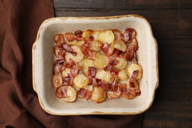 Photo of Delicious baked potatoes and bacon in baking dish on wooden table, top view