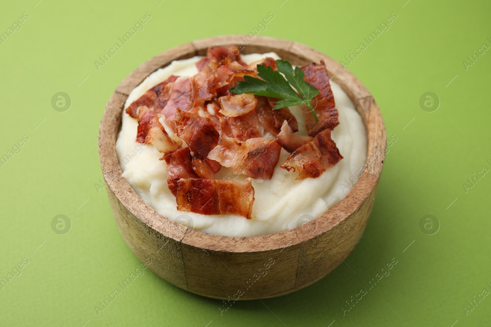 Photo of Fried bacon, mashed potato and parsley in bowl on green background