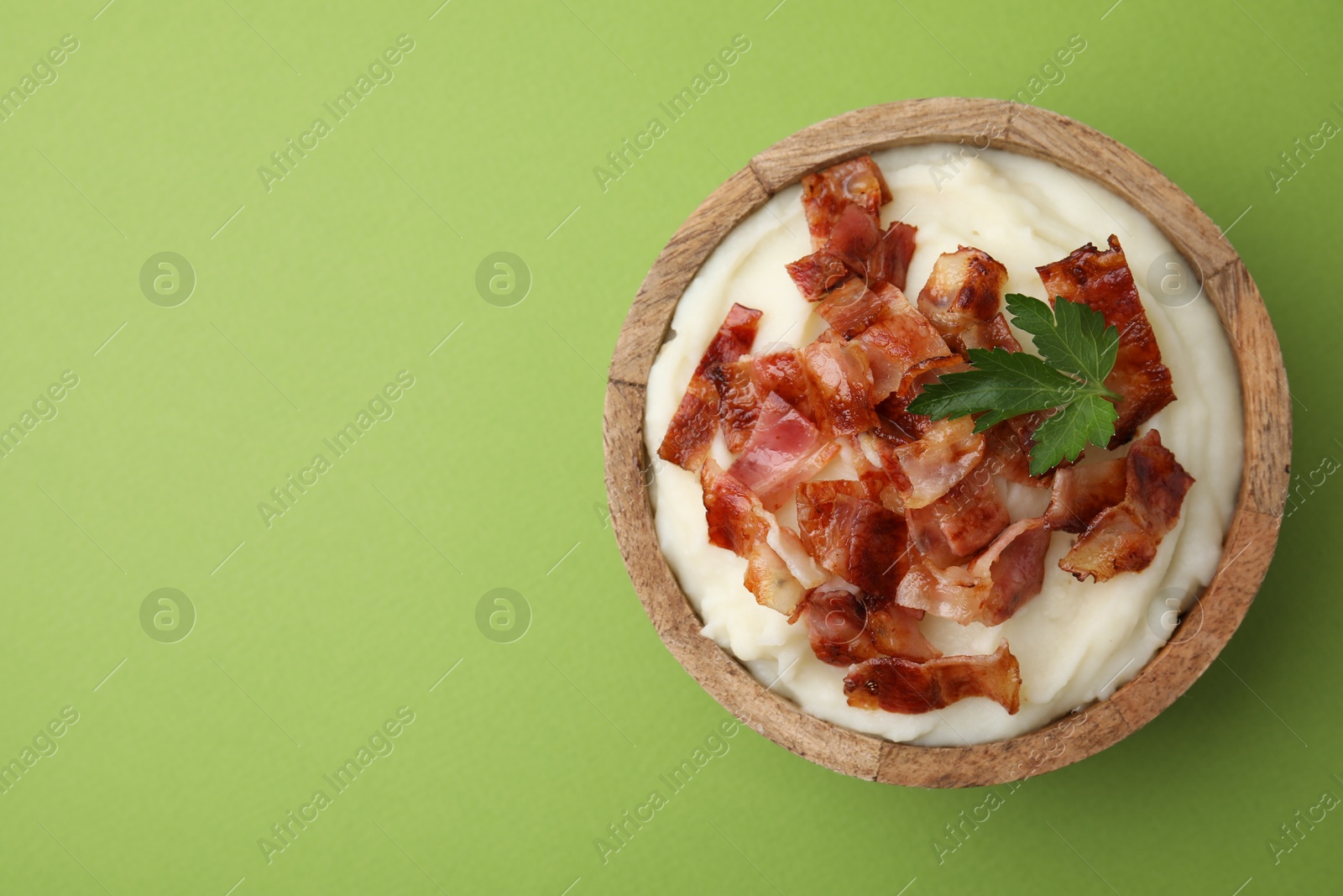 Photo of Fried bacon, mashed potato and parsley in bowl on green background, top view. Space for text