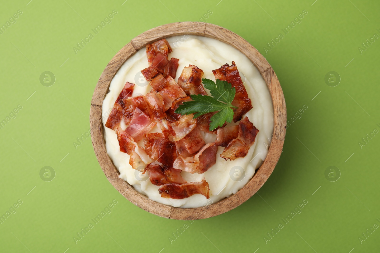 Photo of Fried bacon, mashed potato and parsley in bowl on green background, top view