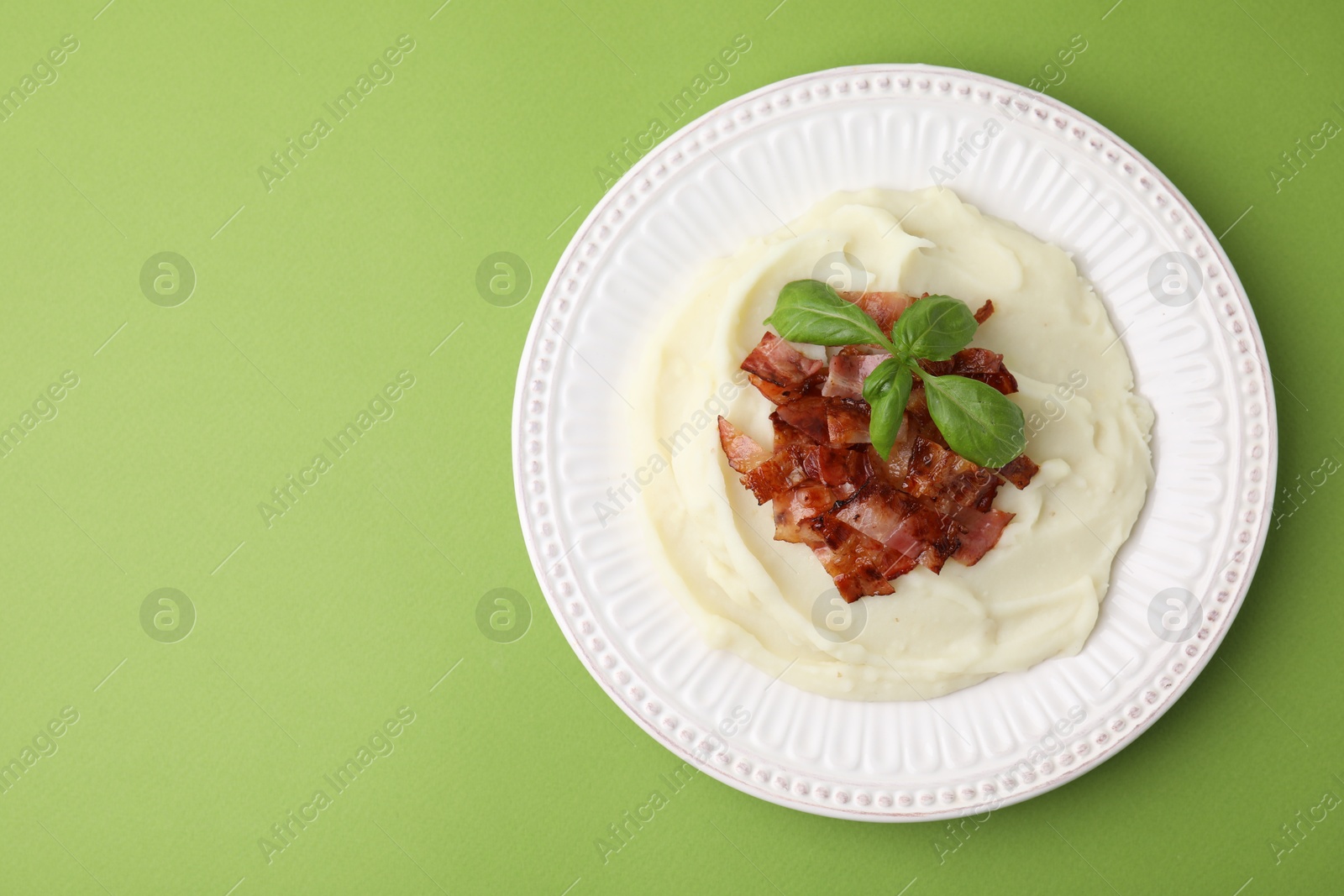 Photo of Fried bacon, mashed potato and basil on green background, top view. Space for text