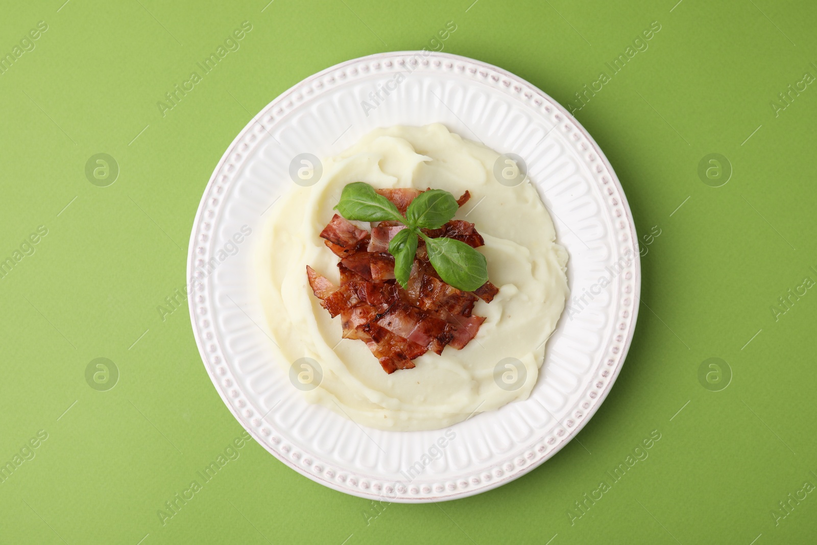 Photo of Fried bacon, mashed potato and basil on green background, top view