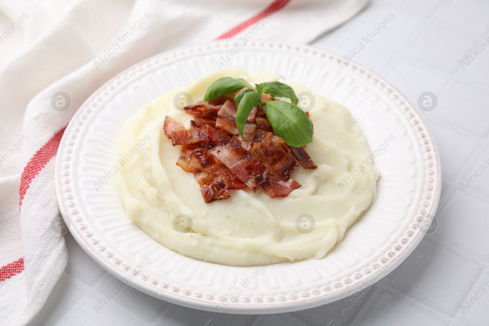 Photo of Fried bacon, mashed potato and basil on white tiled table