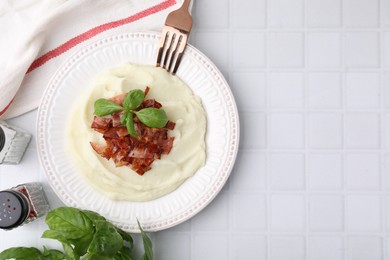 Photo of Fried bacon, mashed potato, basil and fork on white tiled table, top view. Space for text