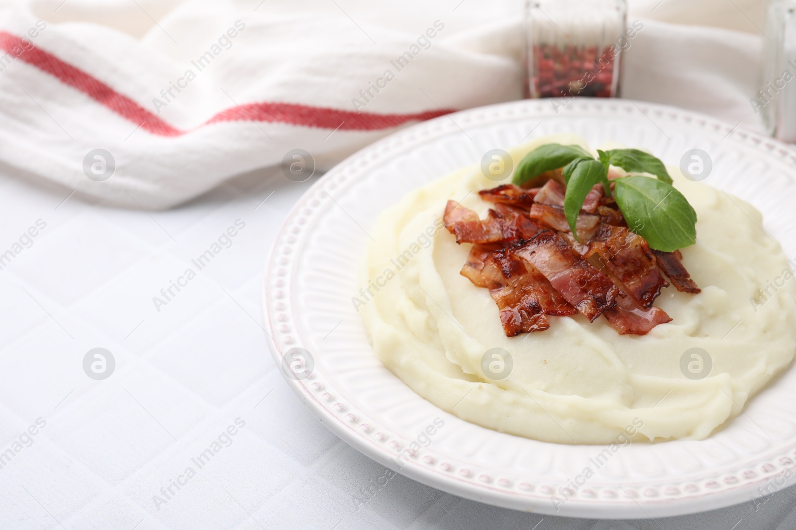 Photo of Fried bacon, mashed potato and basil on white tiled table, space for text