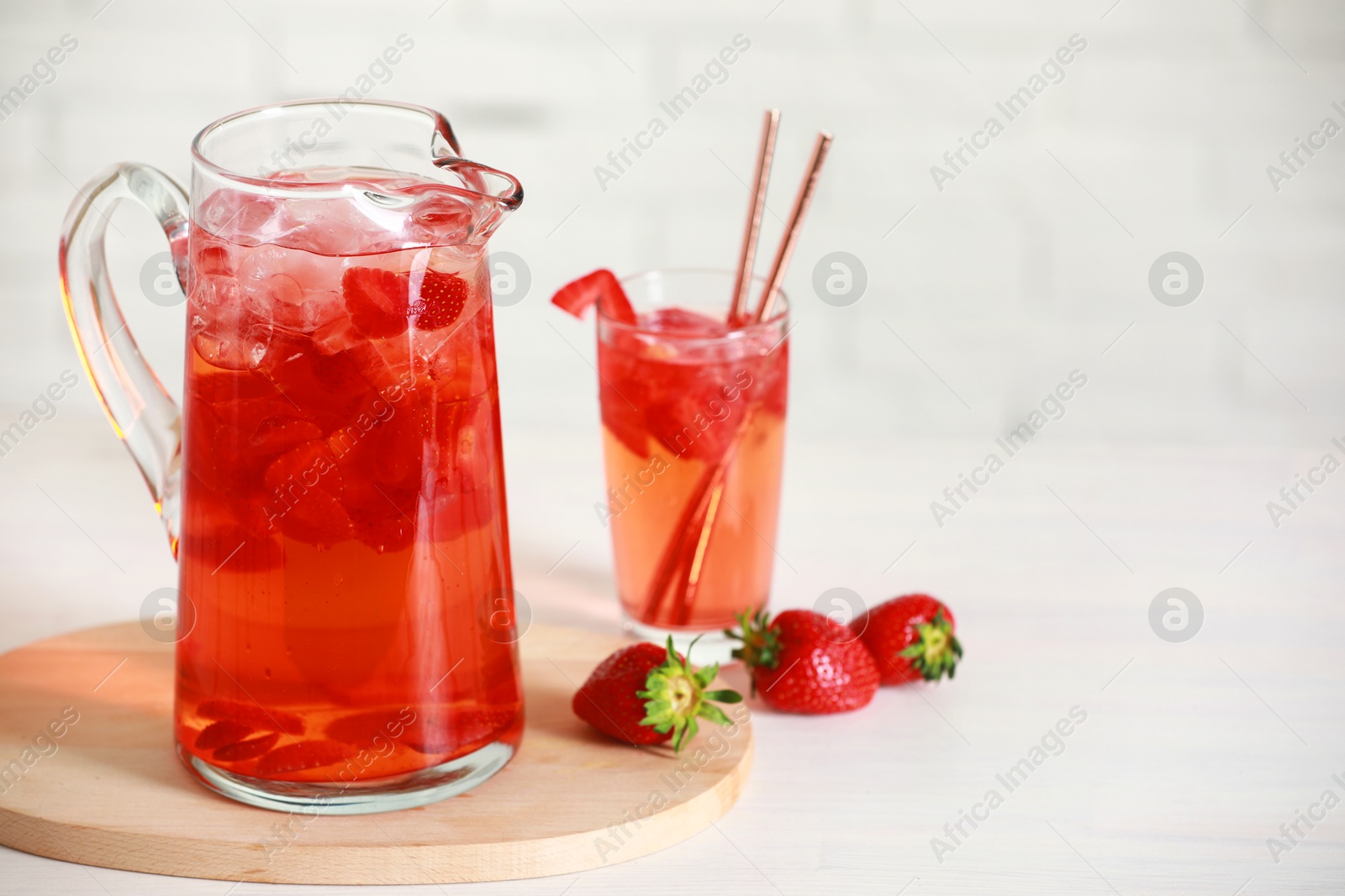 Photo of Tasty strawberry lemonade in jug, glass and berries on white wooden table, space for text